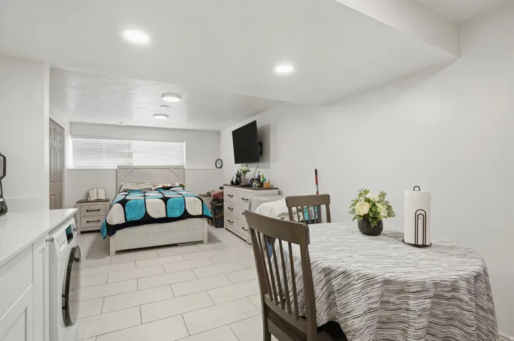 Open-concept space featuring light-toned tile flooring throughout, a built-in countertop with an under-counter washing machine, recessed lighting, and a window with blinds