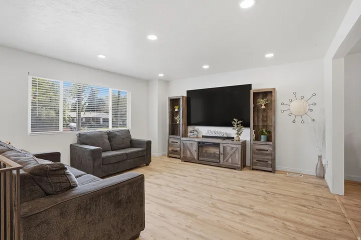 Bright living space featuring wood-finish flooring, recessed lighting, and a large picture window with horizontal blinds