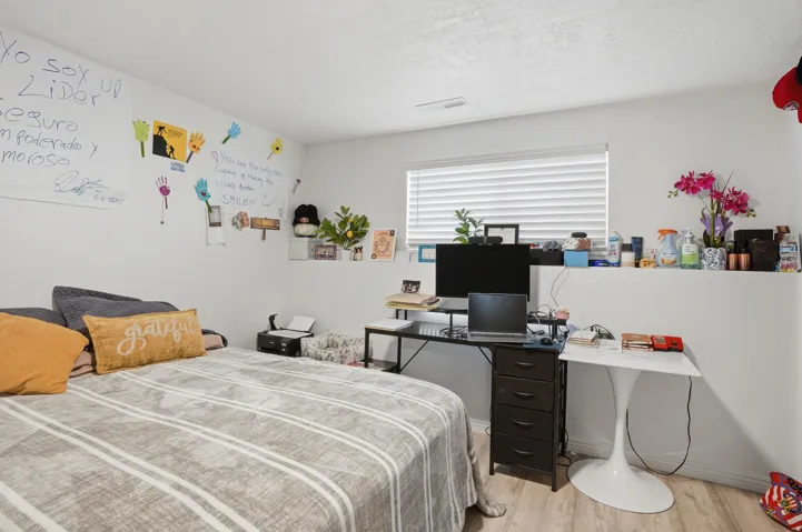 Bedroom featuring light wood-finish flooring, white walls, and a window with blinds