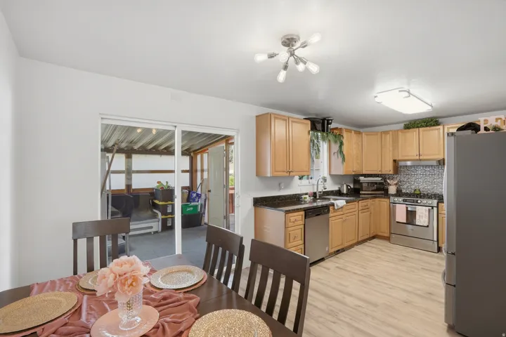 Open concept dining area and kitchen featuring wood-finish flooring, light wood cabinetry, stainless steel appliances, and a tiled backsplash