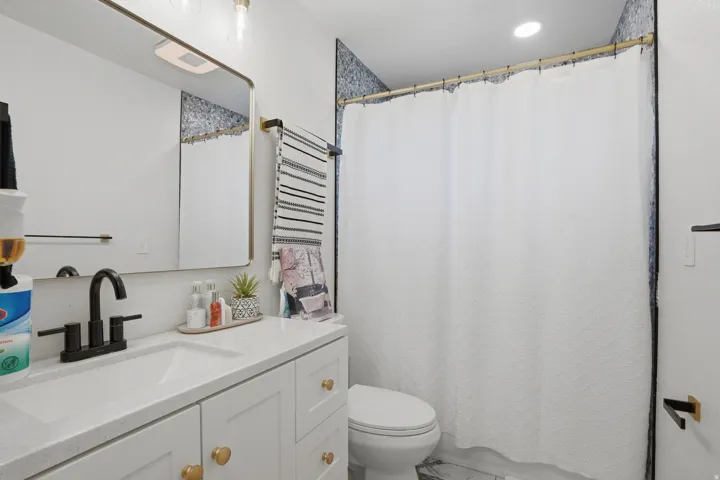 Bathroom featuring a white vanity with gold-toned hardware, a matte black faucet, a framed mirror, and patterned wall tile in the shower area