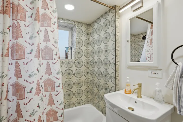 Bathroom featuring a white vanity with an integrated sink, a gold-tone faucet, a mirrored medicine cabinet, and patterned shower tiling