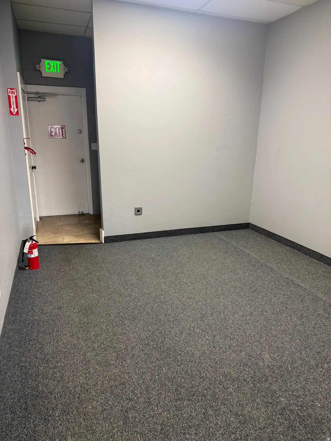 Carpeted interior space with a dropped ceiling and light-toned walls