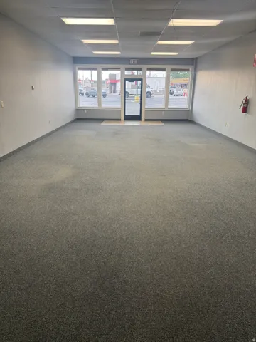 Expansive commercial space featuring broadloom carpeting, a drop ceiling with integrated lighting, and multiple large storefront windows