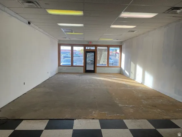 Spacious commercial interior featuring large storefront windows, dropped ceiling with integrated lighting, and a checkered tile entry