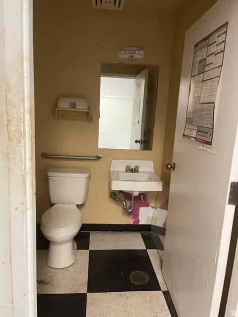 Restroom featuring a wall-mounted sink, white toilet, and black and white checkered flooring