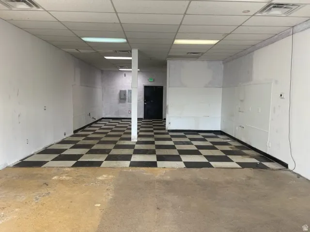 Large interior space featuring a black and white checkered floor pattern, drop ceiling with integrated lighting, and a dark-paneled door