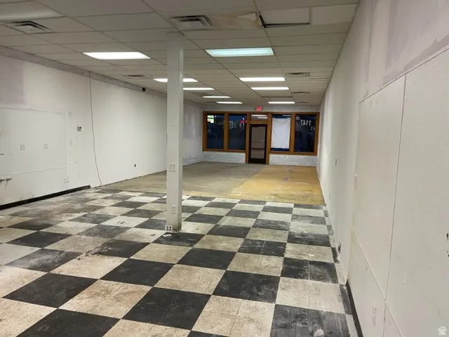 Expansive commercial space featuring a black and white checkered floor, drop ceiling with integrated lighting, and a prominent support pillar