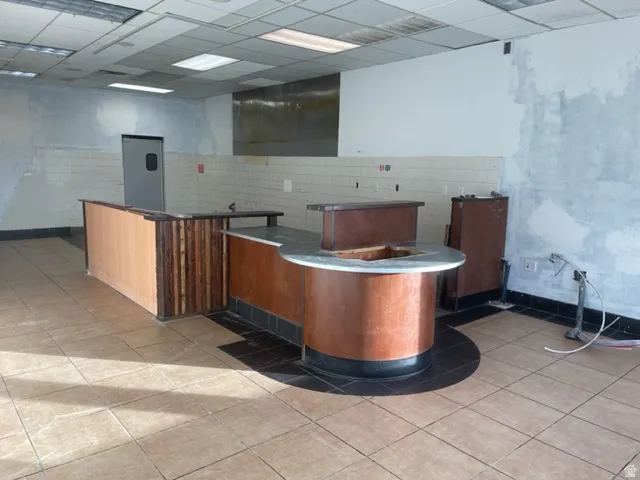 Commercial space featuring a service counter with wood-finish paneling, tiled flooring, and a drop ceiling with integrated lighting
