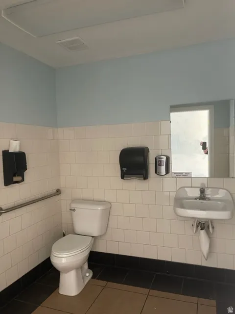 Restroom featuring white square wall tiling, a white toilet, and a white wall-mounted sink
