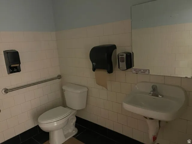 Restroom featuring white subway tile, a wall-mounted sink, and a toilet