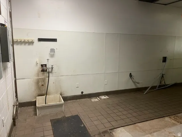 Utility space featuring white paneling, tile flooring, and an exposed utility sink