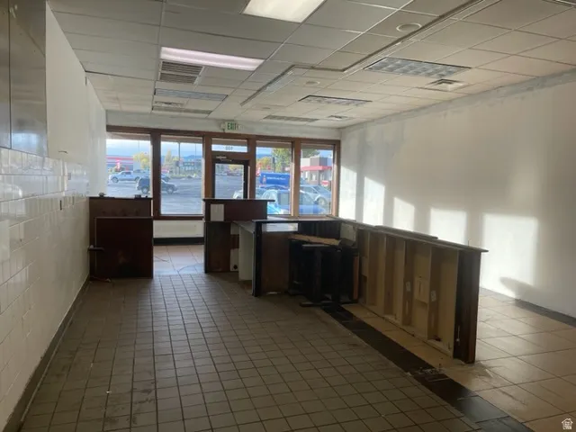 Commercial interior featuring tile flooring, drop ceiling with recessed lighting, and large front windows with wood-finish framing