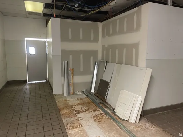 Interior space featuring a utility door with a small rectangular window, drop ceiling with exposed infrastructure, and a mix of tile and concrete flooring