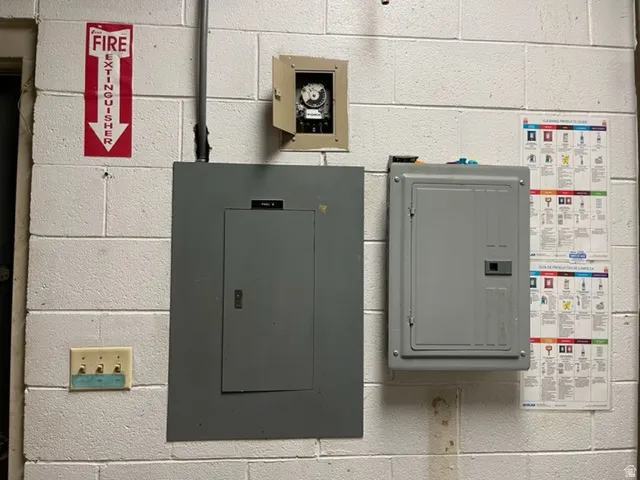 Utility area featuring two electrical panels and an exposed timer unit, mounted on a white cinder block wall