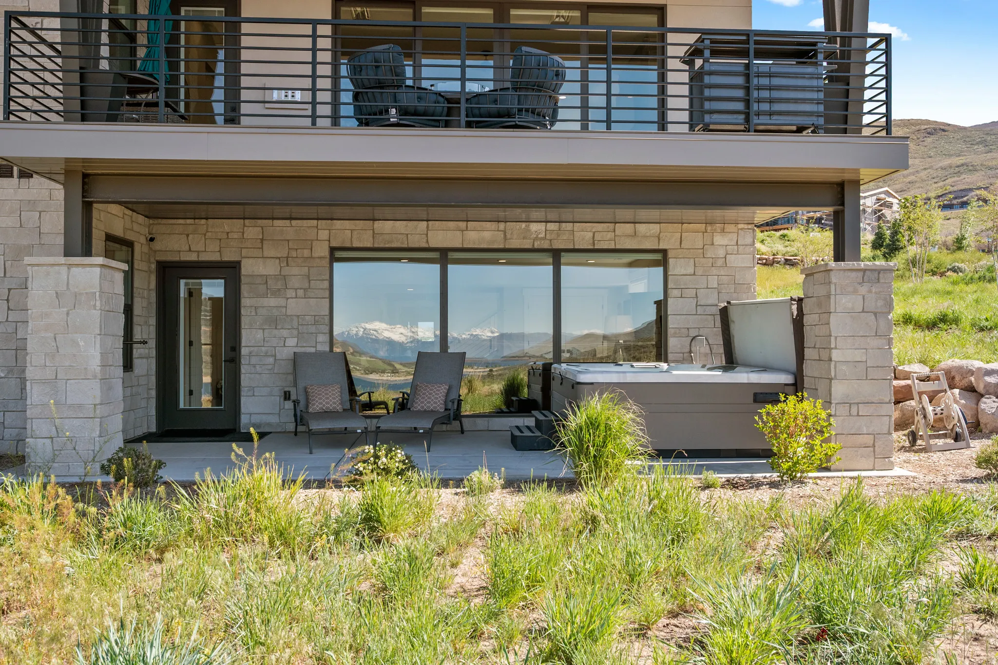 Lower-level patio featuring a spa, stone exterior, and expansive windows