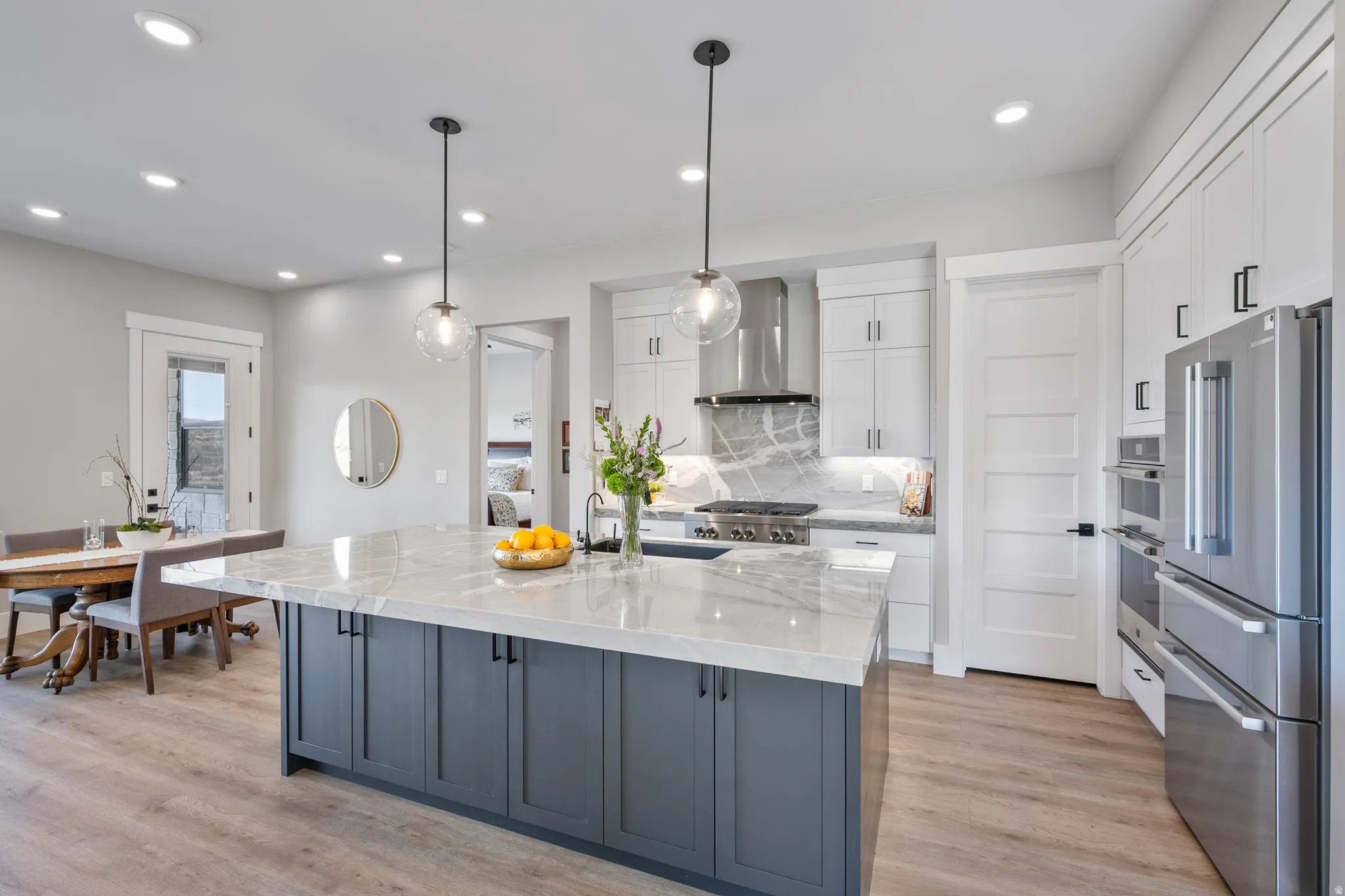 Spacious kitchen featuring a large central island with a light-toned countertop, sleek dark gray cabinetry, and two contemporary pendant lights