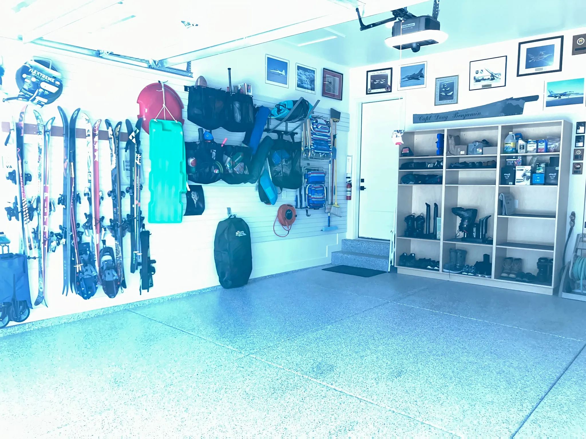 Garage featuring epoxy flooring, built-in shelving, overhead lighting, and wall-mounted storage systems