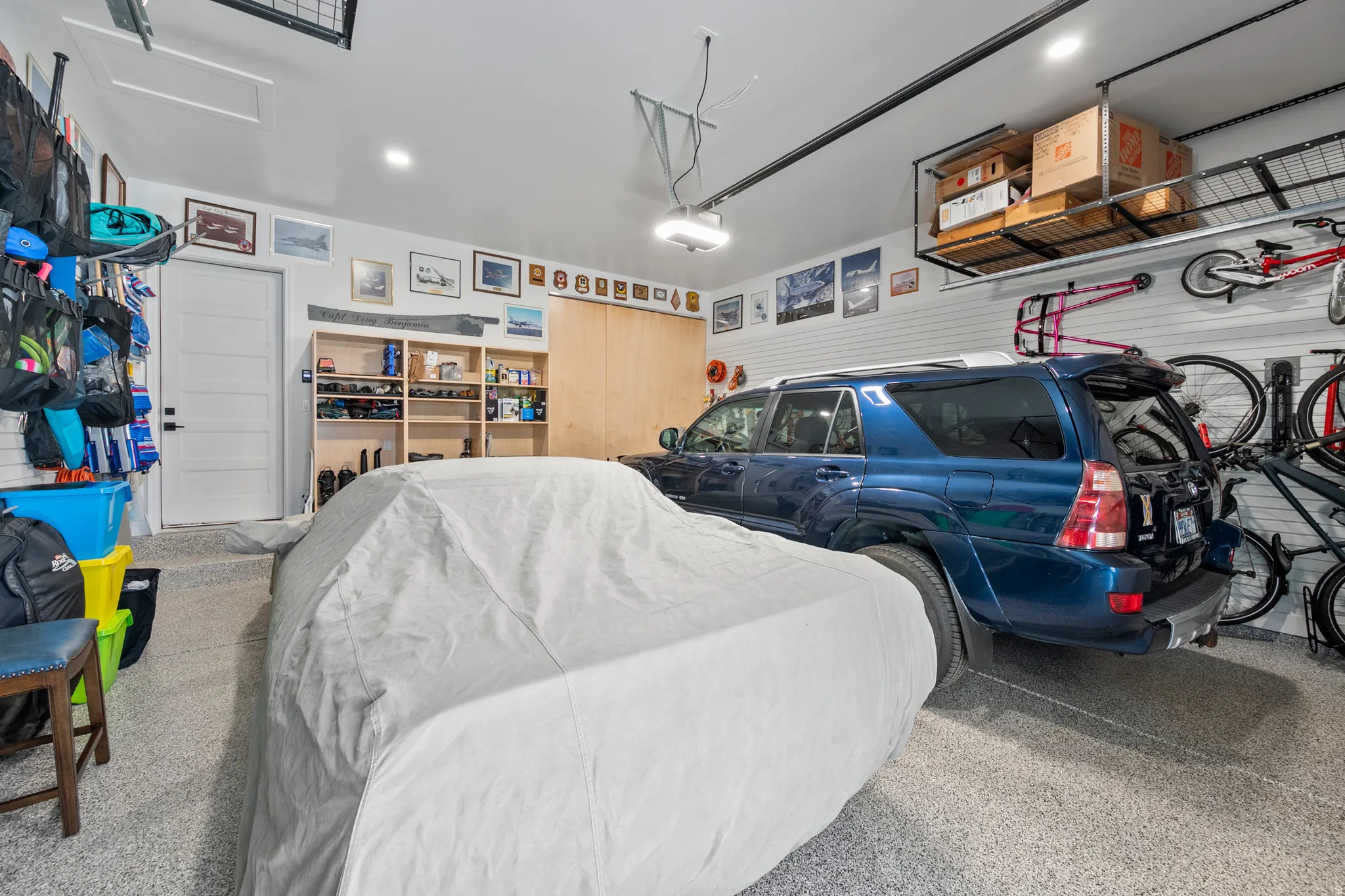 Garage featuring speckled epoxy flooring, built-in shelving, overhead storage racks, slatwall paneling, and an interior access door