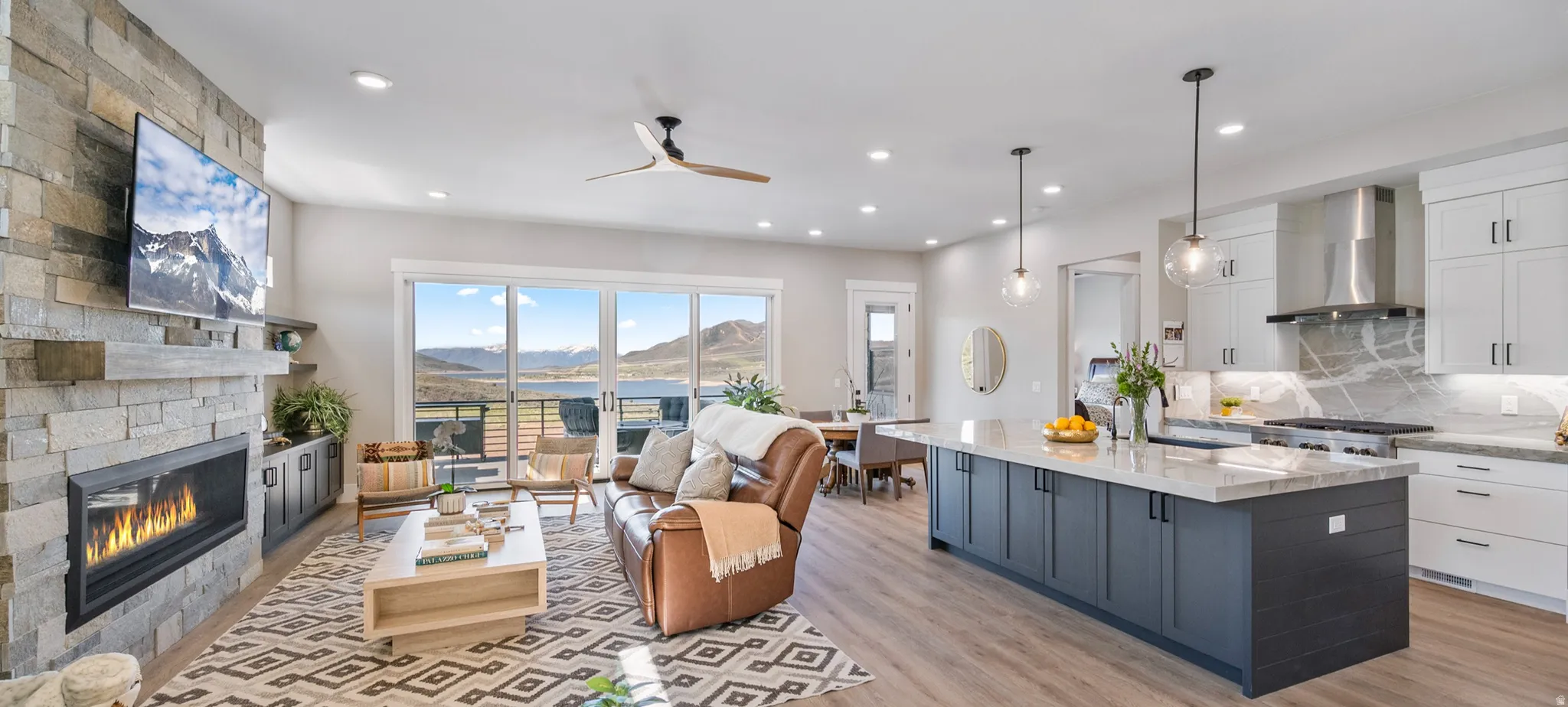 Open-concept living space featuring wood-finish flooring, a stone fireplace with a linear insert, and large sliding glass doors
