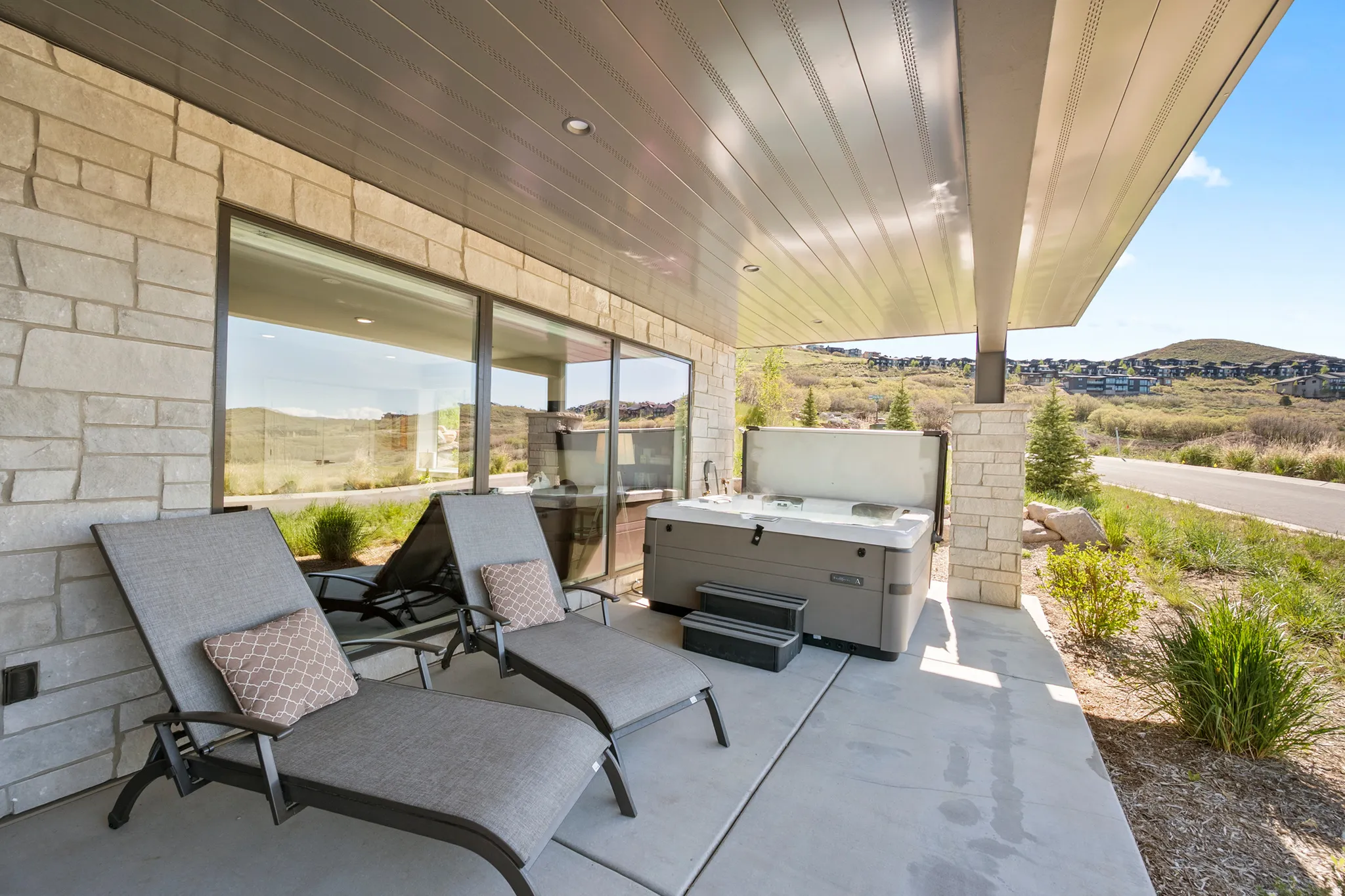 Covered patio featuring a built-in hot tub, concrete flooring, and stone facade