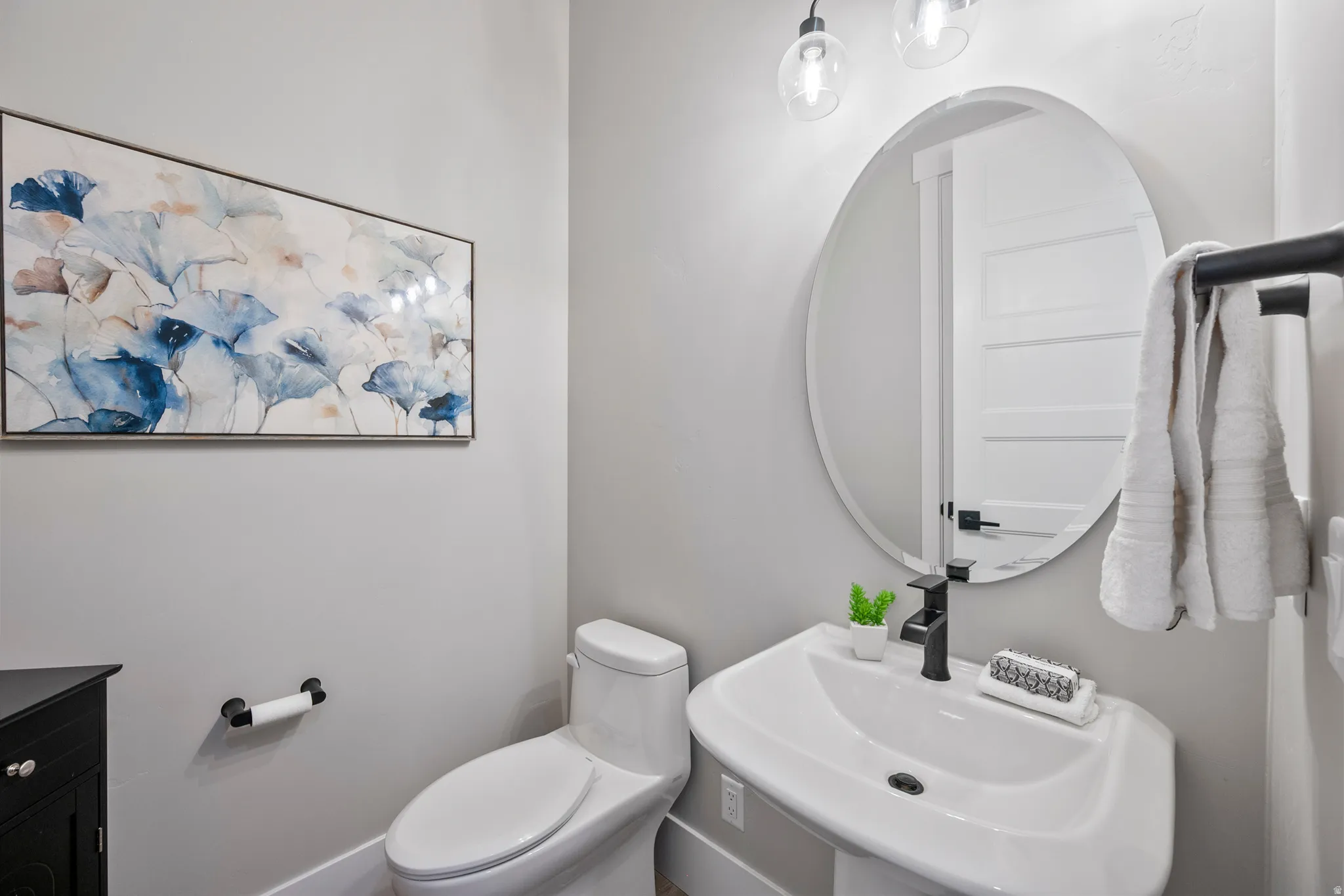 Pedestal sink with matte black faucet, round mirror, and wall-mounted lighting fixtures