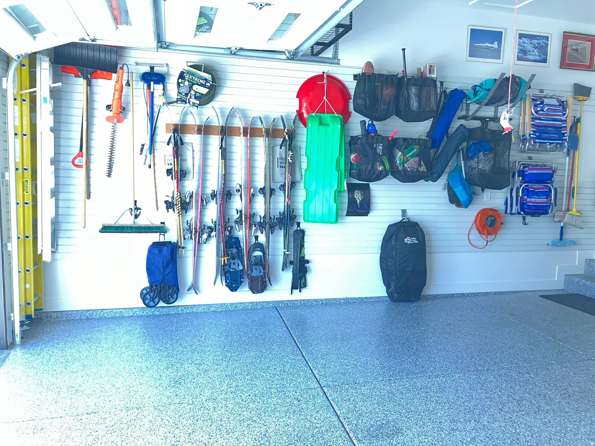Garage featuring a light gray epoxy-coated floor, slatwall organization system, and white painted walls