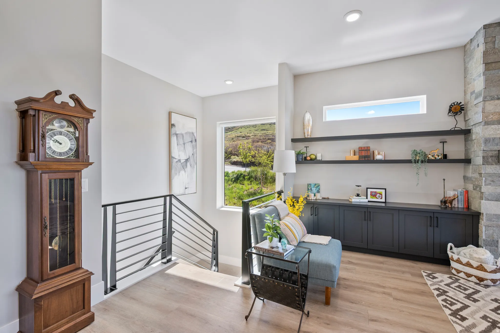 Open landing area featuring wood-finish flooring, a contemporary black metal stair railing, built-in shelving, recessed lighting, and an accent wall with stacked stone detailing