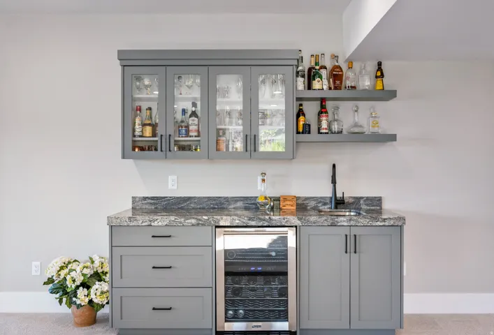 Custom wet bar featuring gray cabinetry, a dark stone countertop, an undermount sink with a matte black faucet, a built-in beverage refrigerator, and open shelving