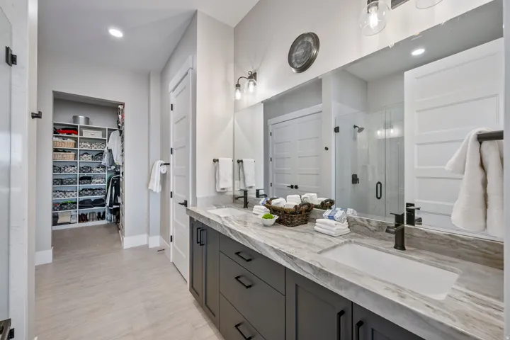Spacious bathroom featuring a dual vanity with integrated sinks, a glass-enclosed shower, a large mirror, and recessed lighting