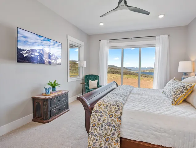 Expansive window wall with sliding glass doors, recessed lighting, ceiling fan, carpet flooring, and a large wall-mounted display