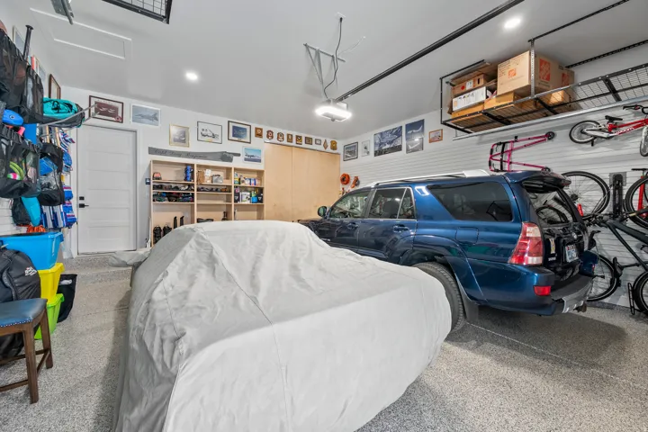 Garage featuring speckled epoxy flooring, built-in shelving, overhead storage racks, slatwall paneling, and an interior access door