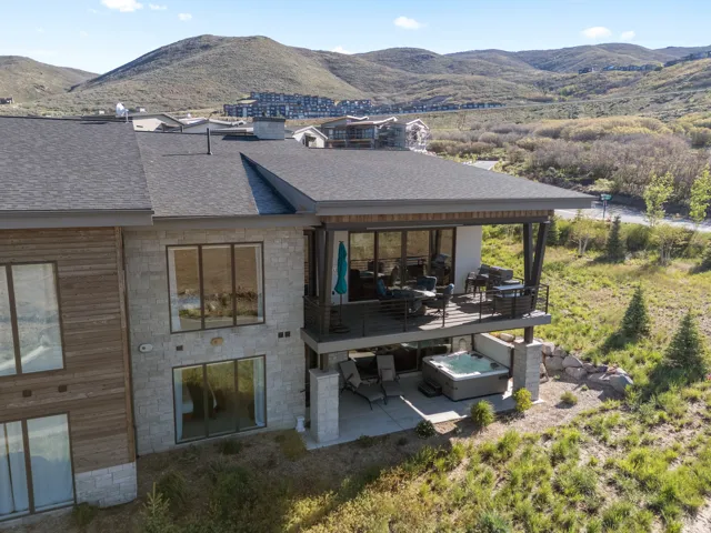 Multi-level exterior featuring a stone and wood facade, covered upper deck with metal railings, lower patio, and an integrated hot tub