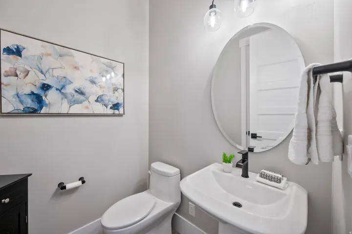 Pedestal sink with matte black faucet, round mirror, and wall-mounted lighting fixtures