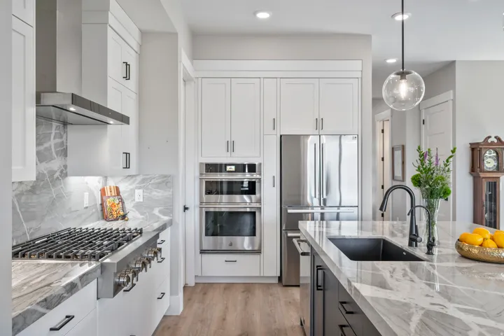 Gourmet kitchen featuring a gas range with stainless steel hood, built-in double ovens, and a side-by-side refrigerator