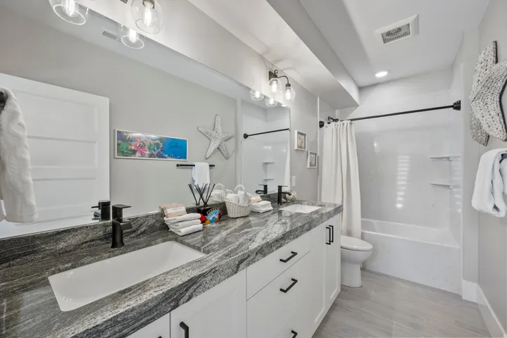 Bathroom featuring a dual vanity with a gray patterned countertop, white undermount sinks, and matte black fixtures