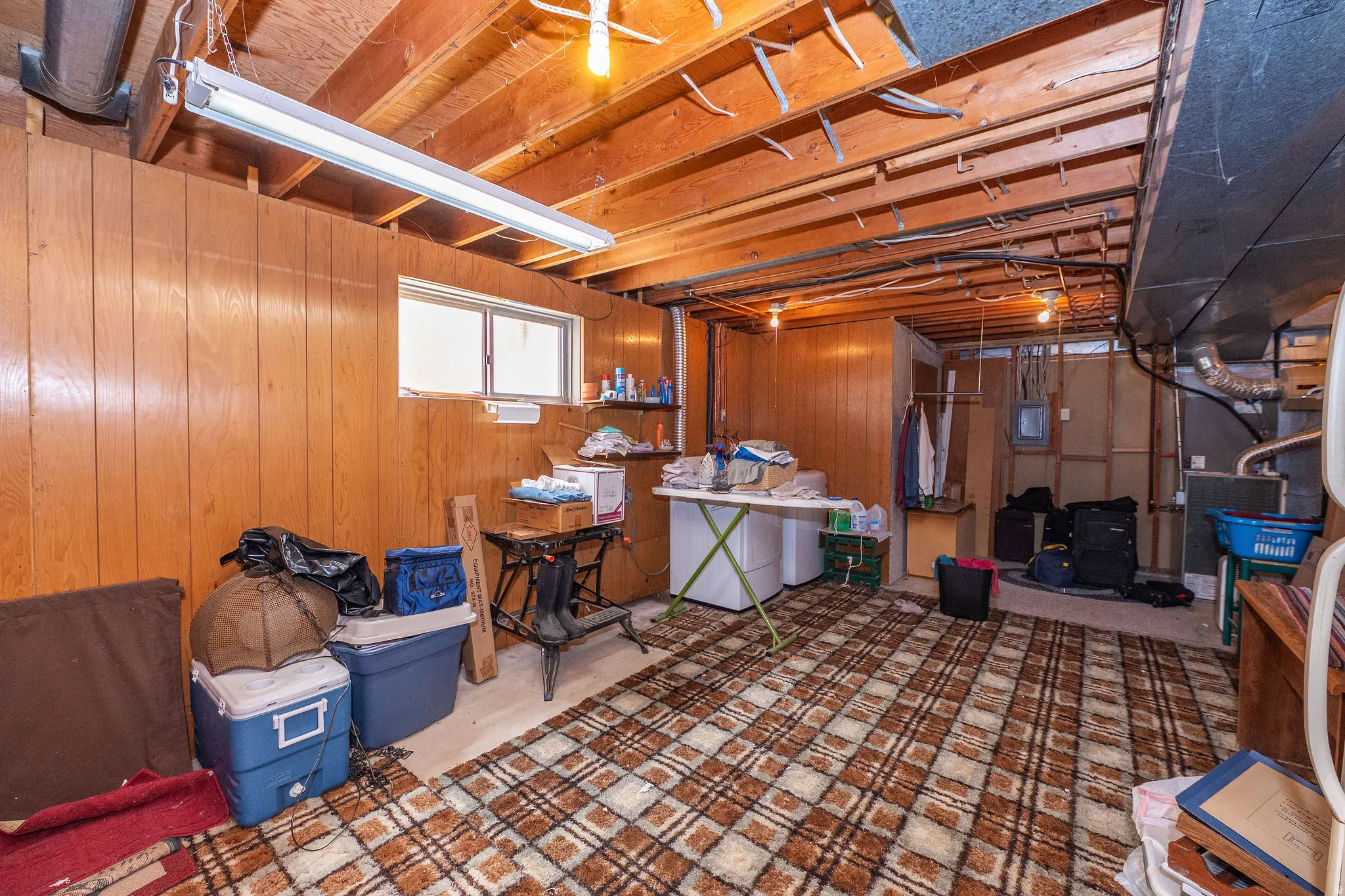 Basement utility space featuring laundry hook ups, wood paneling, exposed ceiling joists, and a window