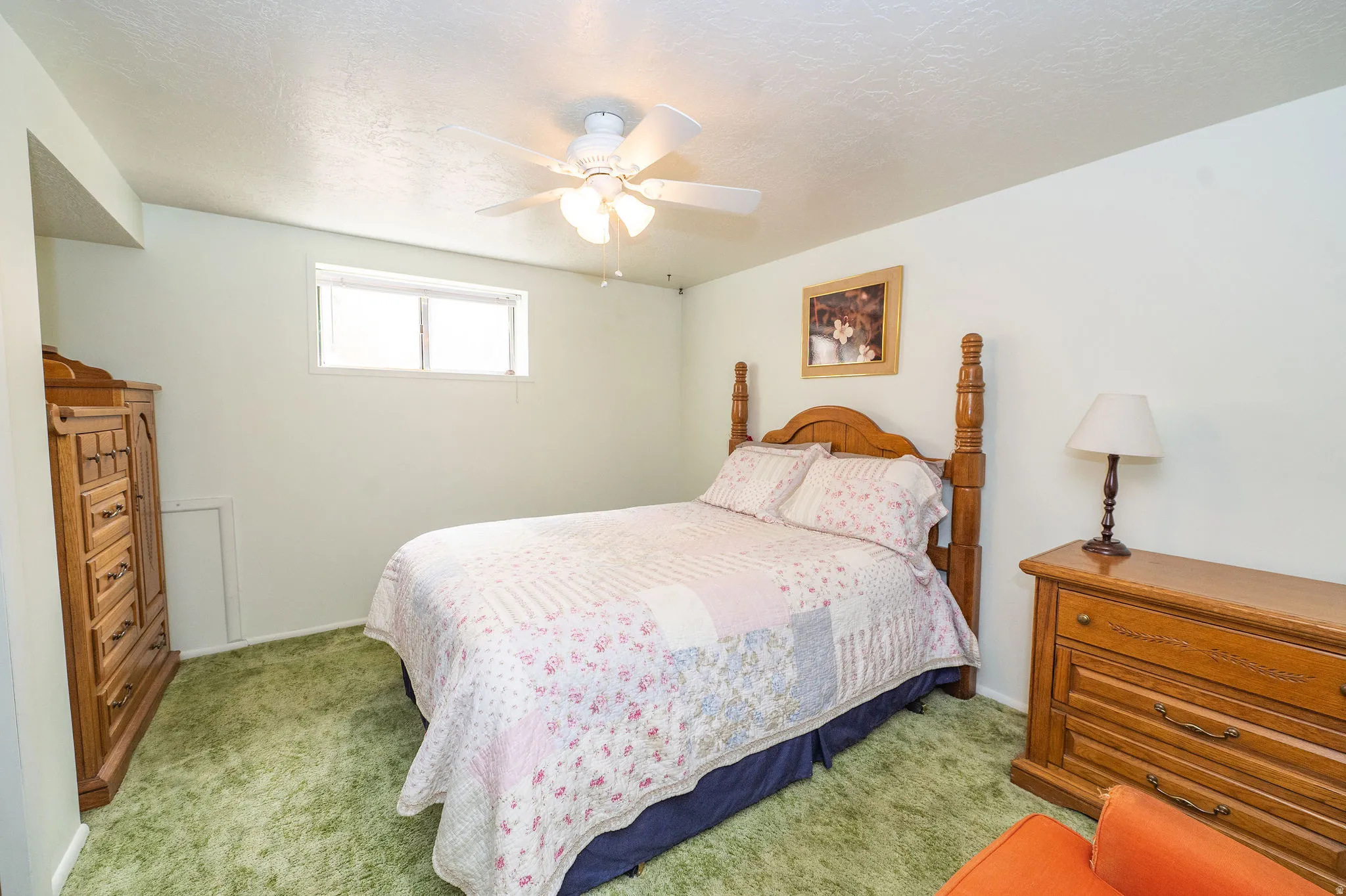 Recessed window with white trim, green carpet flooring, light-colored wall paint, white ceiling fan with light fixture