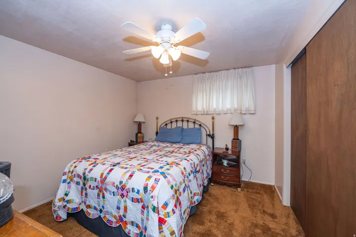 Carpeted bedroom featuring a ceiling fan with light fixture and sliding closet doors