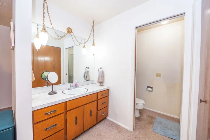 Bathroom vanity featuring a single basin sink, shower, laminate countertop, and wood cabinetry.