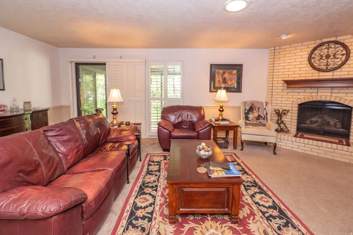 Living area featuring a brick fireplace with a wood mantle, sliding glass doors, white louvered shutters, and recessed ceiling lighting
