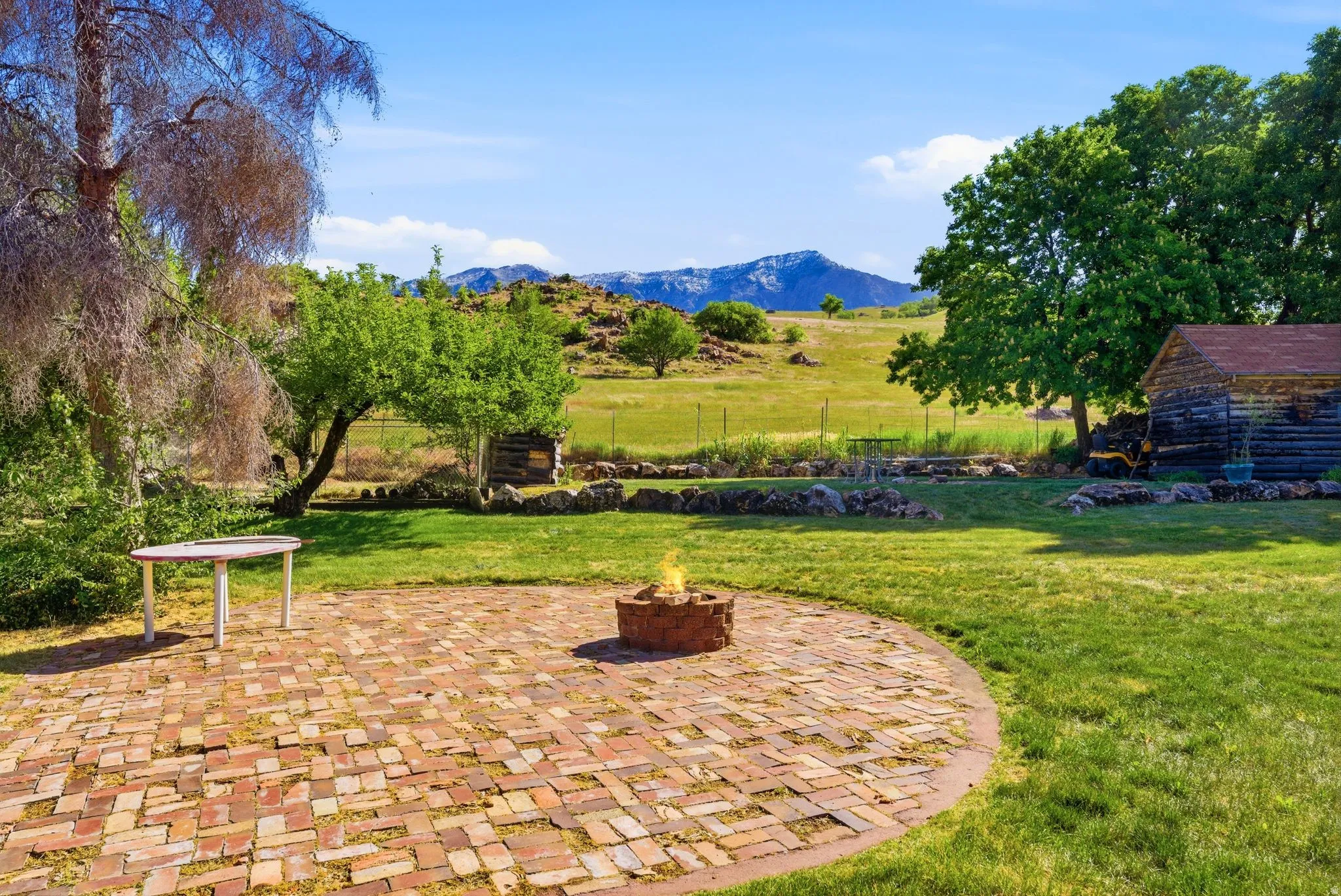 Expansive outdoor space featuring a circular brick paver patio with a built-in fire pit