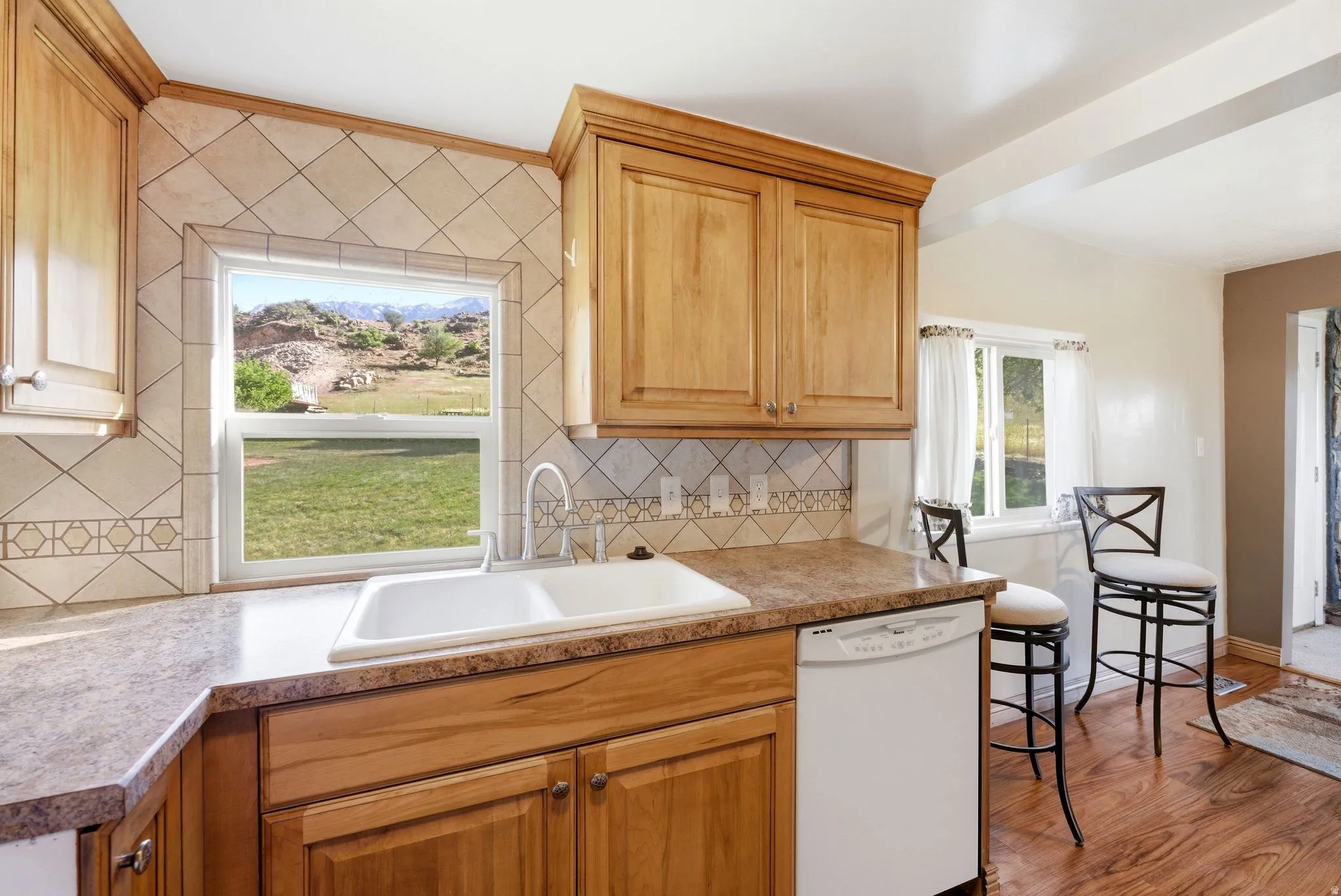 Kitchen featuring light wood cabinetry, a double basin sink, and a white dishwasher