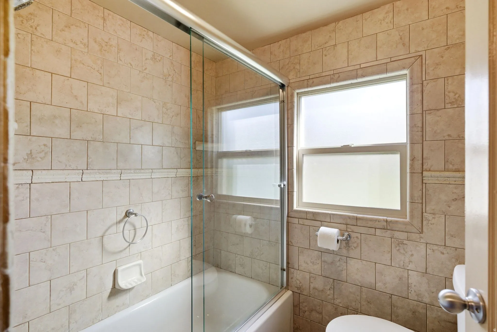 Bathtub with sliding glass enclosure and full-height tiled surround