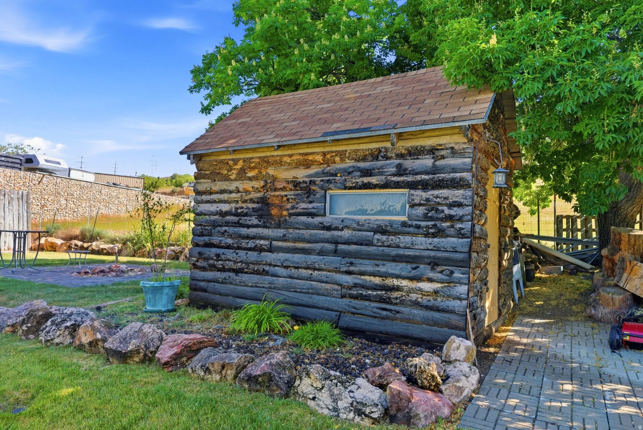 Rustic log-style outbuilding featuring a shingle roof and a horizontal window