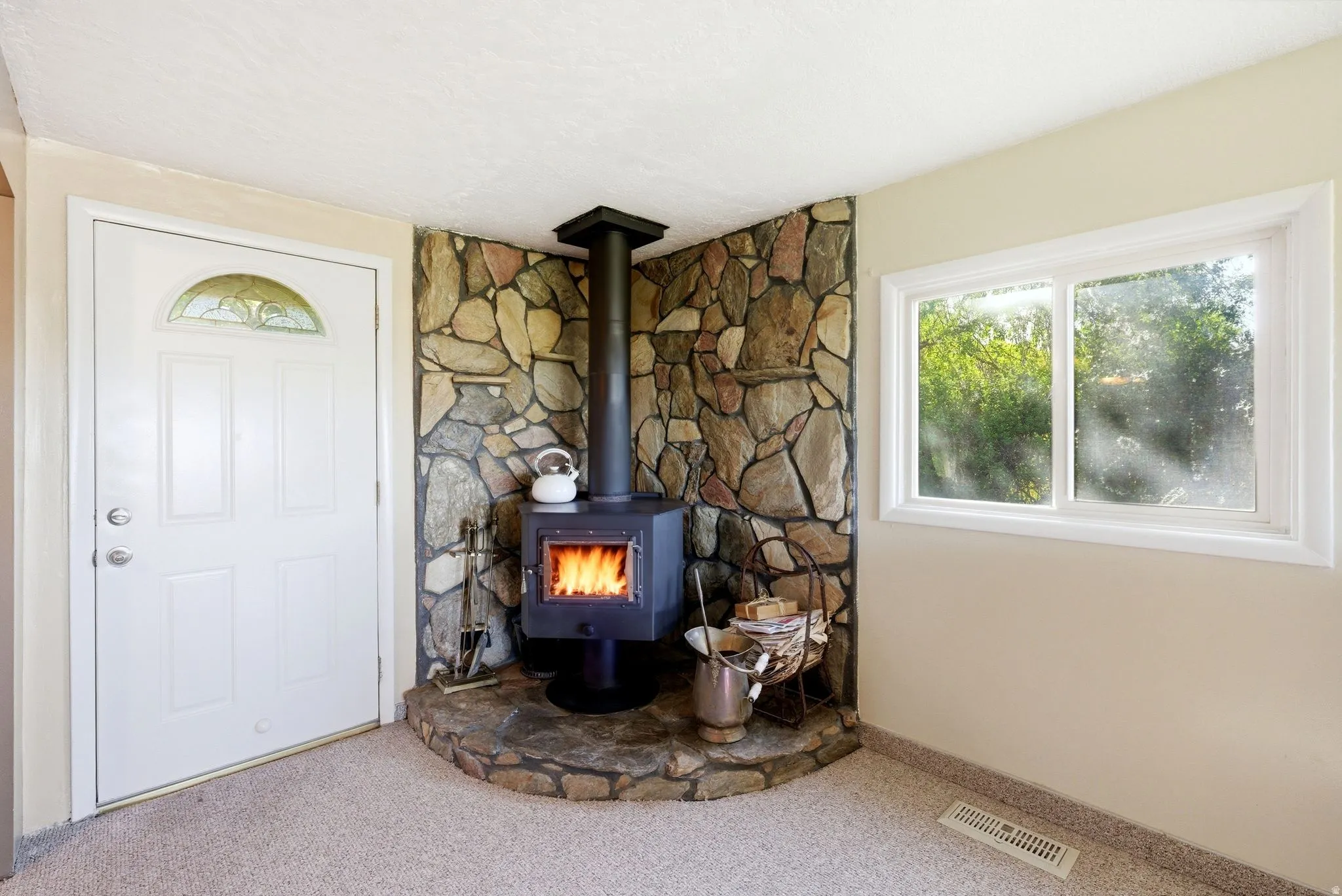 Corner wood-burning stove with a stone surround and hearth, complemented by a white entry door with an arched stained glass insert