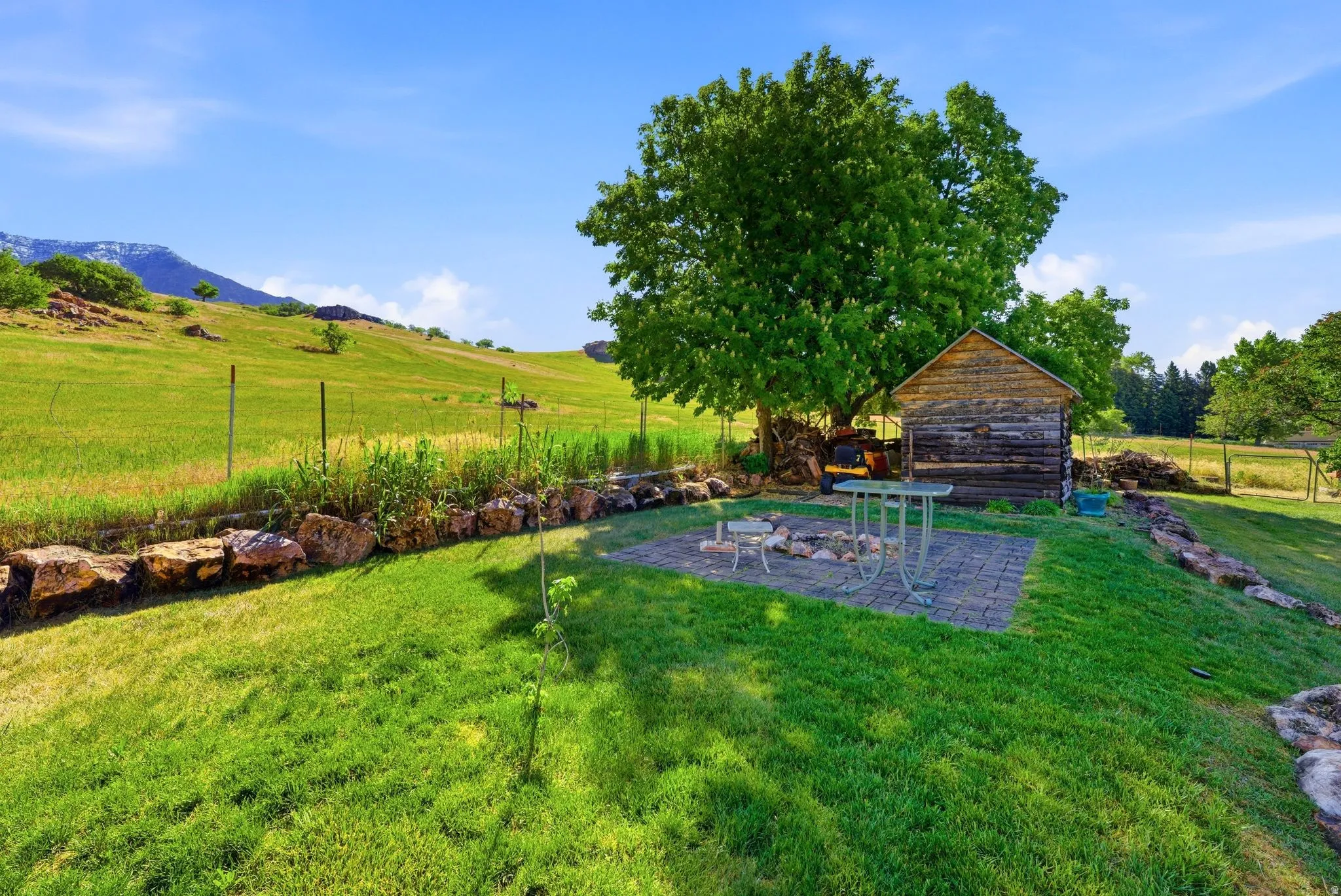 Expansive green lawn featuring a stone retaining wall and a paver patio