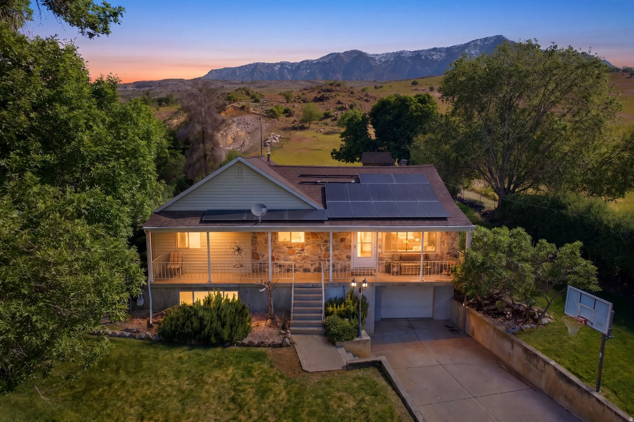 Property featuring an elevated front porch with stone accents, a concrete driveway, a two-car garage, and rooftop solar panels