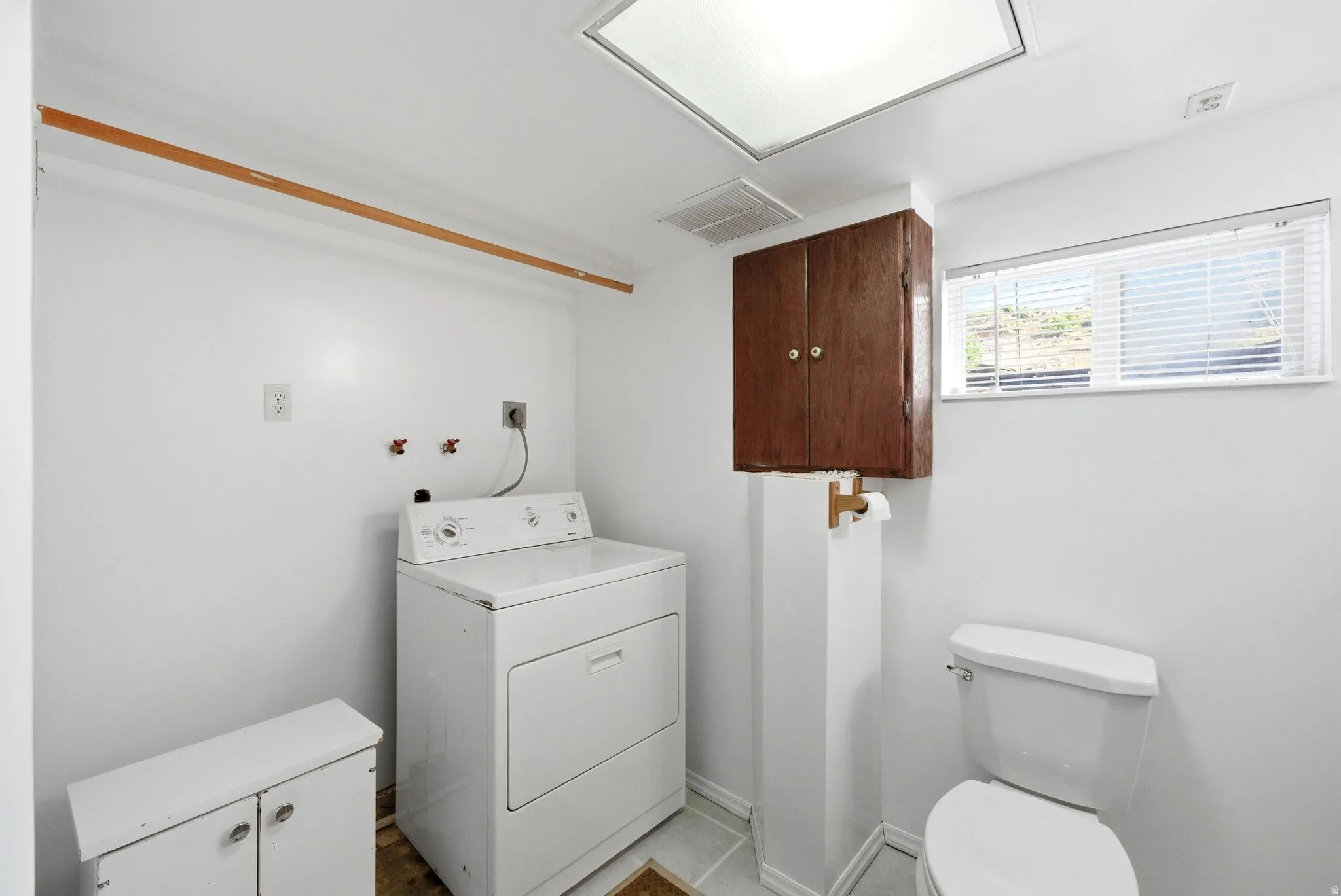 Laundry room with a built-in wooden shelving rod, a large rectangular window with blinds, and tile flooring