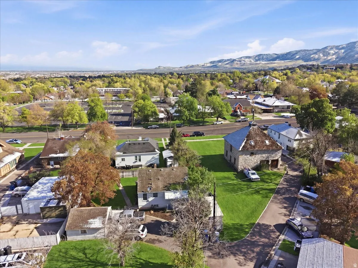 Stone structure with a shingled roof, featuring a surrounding paved driveway and a manicured lawn